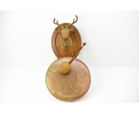 A vintage wall-mounting brass gong, diameter 30cm, suspended from a protruding bronzed stag's head, on oval mount, length 33c