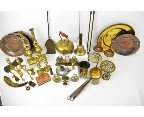 A mixed collection of various brass and copper ware, including a hand bell, candlesticks, fireside tools, a pair of dogs, tri