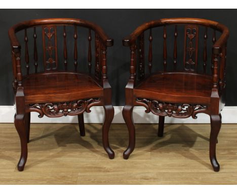 A pair of Chinese hardwood armchairs, horseshoe arm rails above pierced splats and turned spindles, panel seats, shaped apron