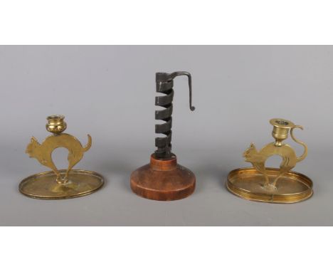 A pair of brass cat-shaped candlesticks, accompanied by a wrought iron Rat De Cave candlestick featuring a cylindrical coiled