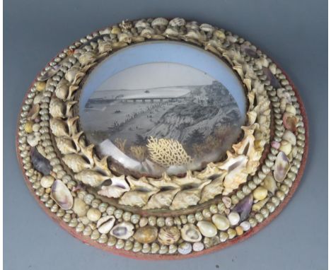 A Victorian engraving of a seaside town with pier, enclosed in a shell and coral decorated frame, 27cm diameter
