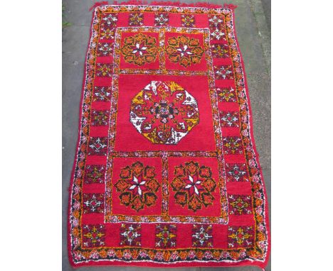 A Moroccan wool rug, the tomato red field with central octagonal medallion, enclosed by four smaller medallions, in a triple 