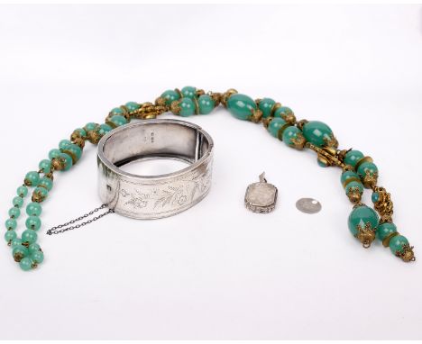 An early 20th century sterling silver bangle bracelet with chased decoration, a white metal locket and a green bead necklace 