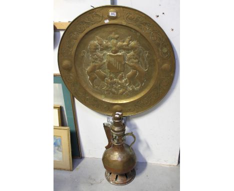 A large vintage Eastern copper kettle with burner underneath, a large brass fly-pressed charger bearing a coat of arms to the