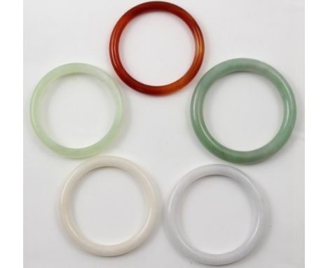 A collection of jade and semi-precious stone bangles comprising two white stone examples, a carnelian-coloured bangle, a cela