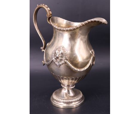 A Victorian silver milk jug, of helmet form raised on a foot and having repoussé and applied cast decoration and a scrolling 