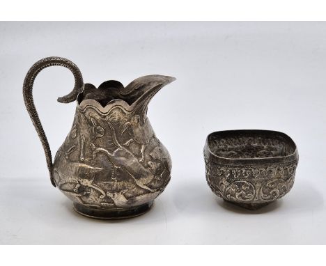 An Indian white metal jug, the side repousse hunting dogs and forest animals, with scroll handle fashioned as a serpent, heig