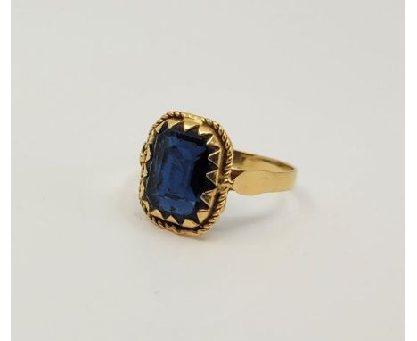 A precious yellow metal and blue paste set cocktail ring, claw set emerald cut blue paste to centre (yellow metal assessed as