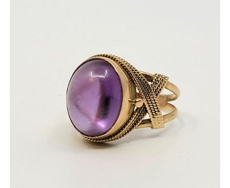 A precious yellow metal and sapphire ring, having oval purple cabochon sapphire in rub over setting with wire work shoulders,