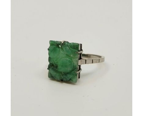 A 9ct. white gold and carved jade ring, claw set carved and pierced rectangular mottled green jade panel, ring size UK N 1/2.