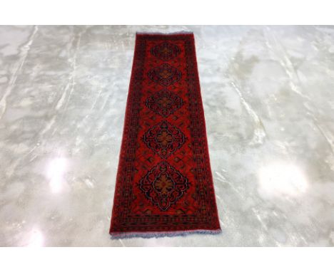 AN AFGHAN WOOL RUNNER (285 x 79cm)
Hand knotted wool with a red field, adorned with repeating octagonal guls, framed by geome