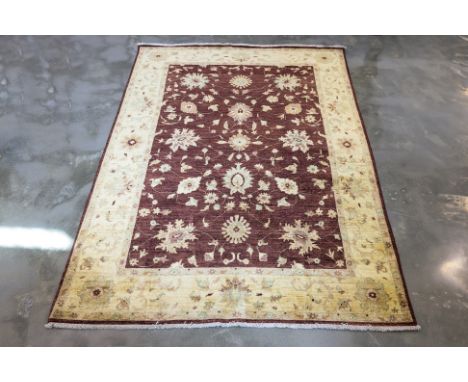 AN AFGHAN WOOL RUG (263 x 180cm) Hand knotted wool pile with a burgundy field adorned with floral motifs, framed by a contras