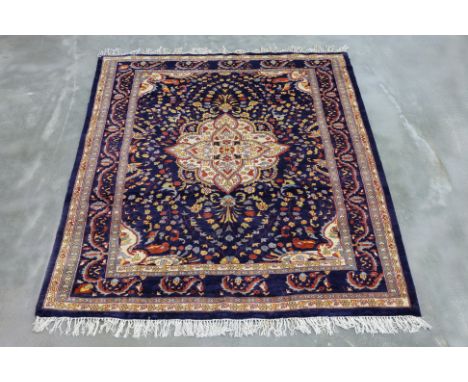 A SAROUK WOOL RUG (176 x 156cm)
Hand knotted wool, dark navy field with a central floral medallion in cream, red, and gold to