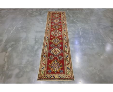 A KAZAK WOOL RUNNER (324 x 83cm)
Hand knotted wool pile with geometric medallions in red, ivory, and blue, surrounded by a na