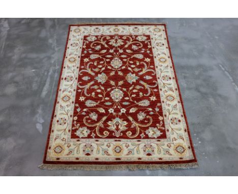 AN AFGHAN REZA WOOL RUG (192 x 125cm)
Hand knotted wool pile with a floral vine pattern on a deep red field, and a light crea