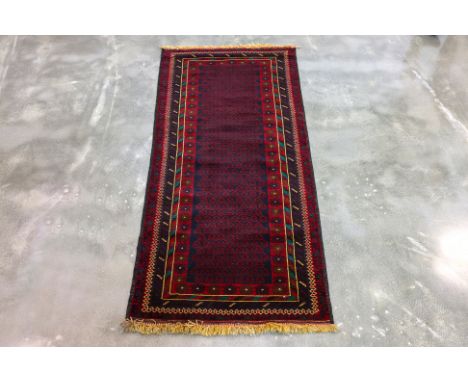 A PERSIAN WOOL RUNNER (188 x 83cm)
Hand knotted wool pile with a red and indigo field, octagonal gul motifs, starburst rosett