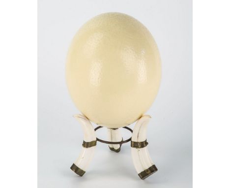 A decorative ostrich egg, blown shell supported on a tripod tusk stand, 9.5in. (24.2cm.) high including stand.
* CONDITION: I