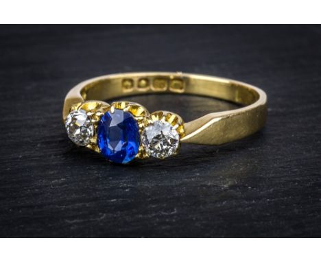 An Art Deco period 18ct gold, sapphire and diamond three stone ring, the central oval cut cornflower blue sapphire flanked by