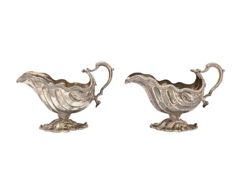 A pair of George II rococo silver sauceboats, shell shaped with gadrooned rim and leaf capped scaly handle, on conforming cas