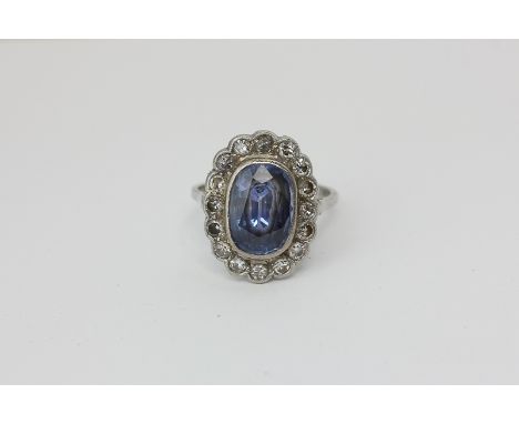 A sapphire and diamond cluster ring, the oval cut stone within a border of sixteen round diamonds in platinum