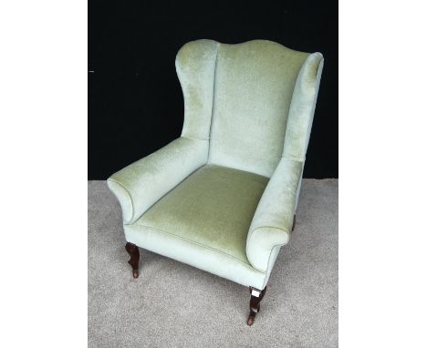 Wingback armchair, the scroll arms and sprung seat raised on cabriole legs terminating in pointed pad feet and ceramic caster