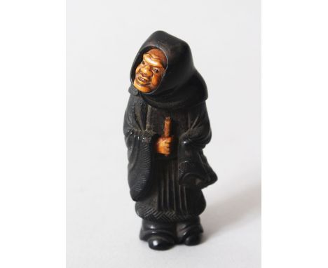 A JAPANESE MEIJI PERIOD CARVED EBONY NETSUKE OF A FIGURE, the figure stood wearing a cowl, the face and hands in lighter timb