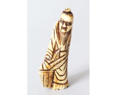 A JAPANESE EDOI PERIOD CARVED STAG ANTLER NETSUKE OF GENKEI SENNIN, the sennin stood holding a leaf aside a basket, himotoshi