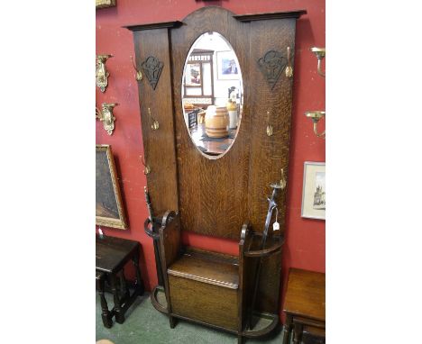 An Arts and Crafts oak hall stand, oval bevel edge mirror flanked by Bakelite cartouches and brass hooks, storage with hinged