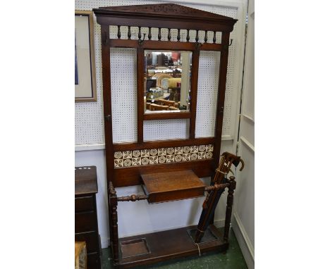 A late Victorian oak hallstand, architectural pediment, spindled back over rectangular plate, tile back above glove box, turn