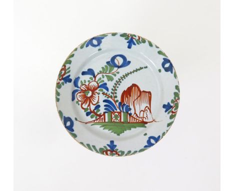 A Bristol delftware plate  c.1740, boldly painted in blue, red and green with Oriental flowers and willow issuing from a fenc