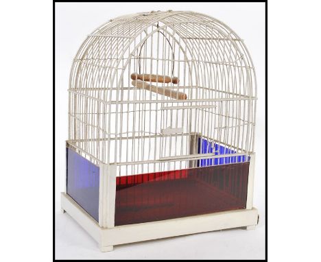 A vintage 20th Century bird cage having white bars and a wooden perch to the interior with blue and red glass panels. 40cm hi