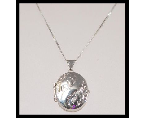 A stamped 375 white gold necklace with a spring ring clasp having a oval form locket with foliate engraving. Weight approx 4.