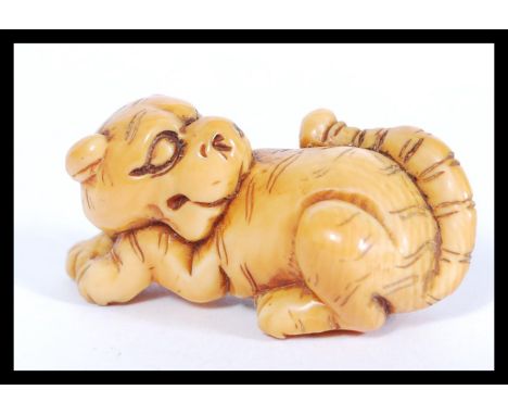A rare Meiji period ivory Netsuke of a crouching tiger, its head turned back with long striped tail and body. Nice colour and