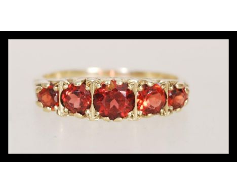 A hallmarked 9ct gold five stone ring having graduating faceted red stones in scrolled mount. Weighs 3.6 grams size V.