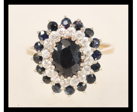 A hallmarked 9ct gold ring set with a an oval cut blue sapphire within a halo of white and stones and blue sapphires. Hallmar