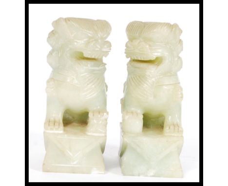 A pair of vintage 20th Century Chinese carved green stone fu dogs, the dogs in seated position raised on square pedestal supp