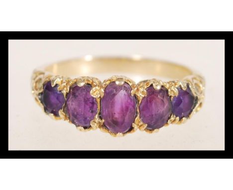 A hallmarked 9ct gold ring set with five oval purple stones with decorative scrolled shoulders. Weight 2.7g. Size O.5.