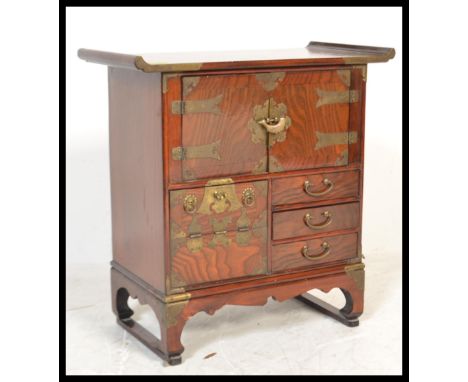 A Chinese table top elm side cabinet of altar shape raised on bracket base with brass bound sides, drawers and drop fronts.&n