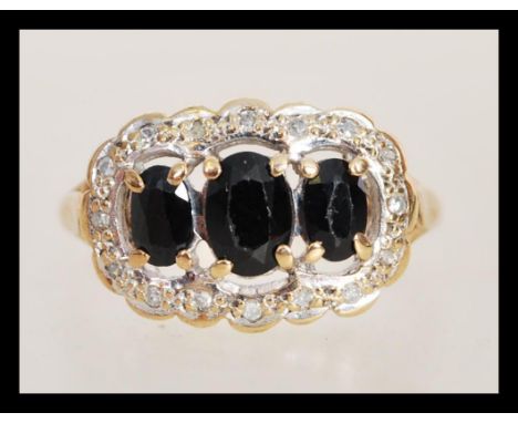 A hallmarked 9ct three stone sapphire ring having three faceted sapphires in prong settings with a halo of illusion set diamo