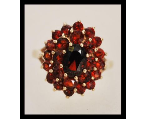 A hallmarked 9ct gold ring having a central faceted red stone with two halos of smaller faceted red stones. Weighs 3.3 grams 