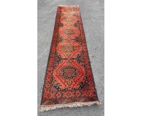 A 20th century runner rug, on a light and dark red ground, with five central motifs and repeating border, 383cm x 84cm 