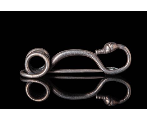 Ca. 450 - 350 BC. A silver brooch formed from a round-section rod, shaped into a sinuous shape with a tightly coiled catch pl