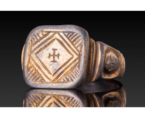 Ca. 1200 - 1400. A silver-gilt ring with a flat, square-shaped bezel engraved with a central cross potent framed by a double 