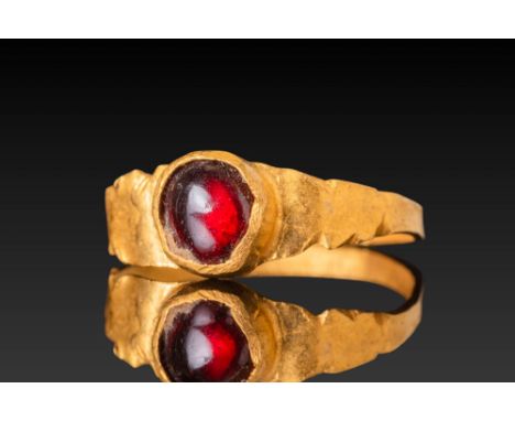 Ca. AD 400 - 600.A gold ring with a red garnet cabochon set in a rounded bezel. The hoop is hammered flat and flares at the s