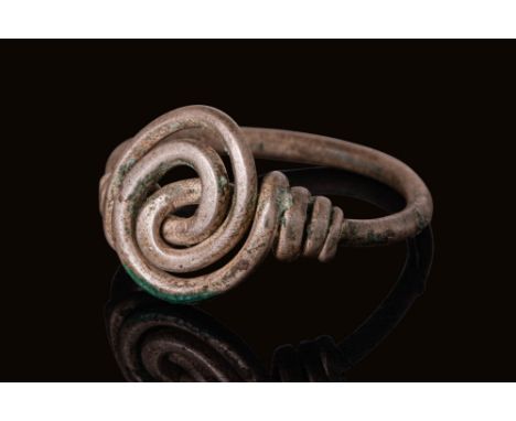 Ca. AD 500 - 700. A silver ring formed from a single round-sectioned wire shaped into an openwork spiral motif at the bezel. 