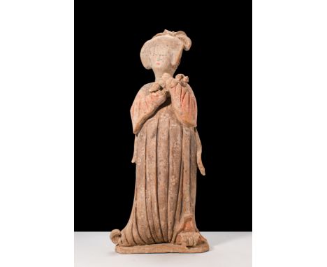 Ca. AD 619 - 907.A terracotta court lady holding a small dog. She stands upright with hands clasped to the chest, cradling th