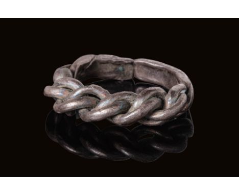 Ca. AD 900 - 1000. A silver ring with a plain, rounded hoop that transitions into a thick, three-strand braid forming the bez
