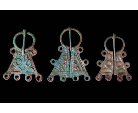 Ca. AD 575 - 625. A collection of three bronze brooches, each comprising matched triangular halves linked by a rounded shank 
