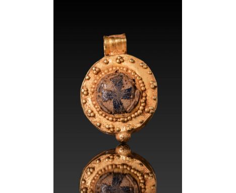 Ca. AD 400 - 600. A gold pendant of circular form with a raised glass inlay at the centre enclosing a dark-toned cross. The i