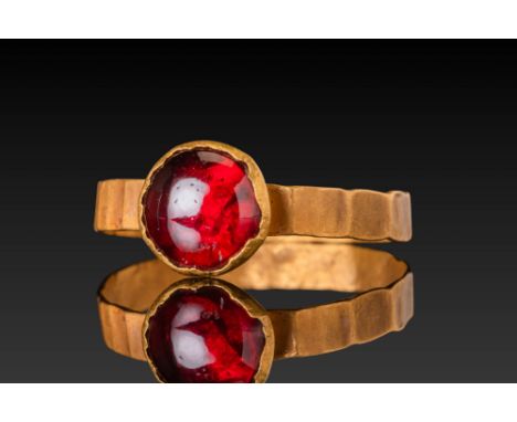 Ca. AD 400 - 600.A gold ring set with a circular red garnet cabochon in a round bezel. The hoop is flat, with lightly indente